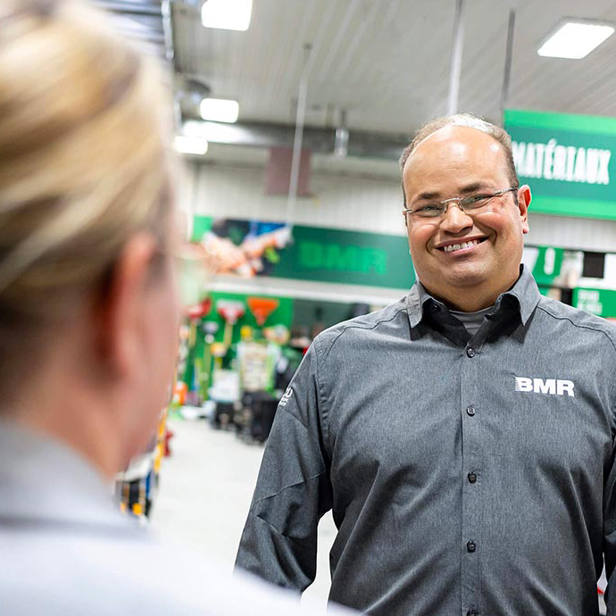 Employé de BMR souriant en chemise grise avec logo.